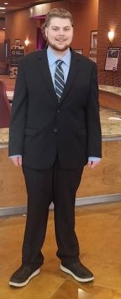 It's a picture of Chase Lathrop he is standing inside of a building. Wearing a suit and tie and rocking the mullet. 